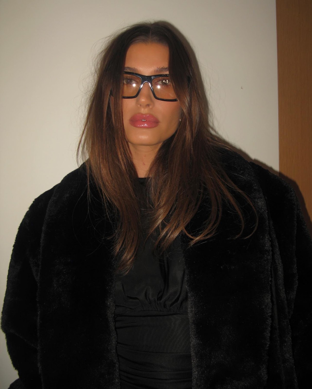 Woman with highlighted blonde hair wearing black fur coat and thick black eyeglasses frames