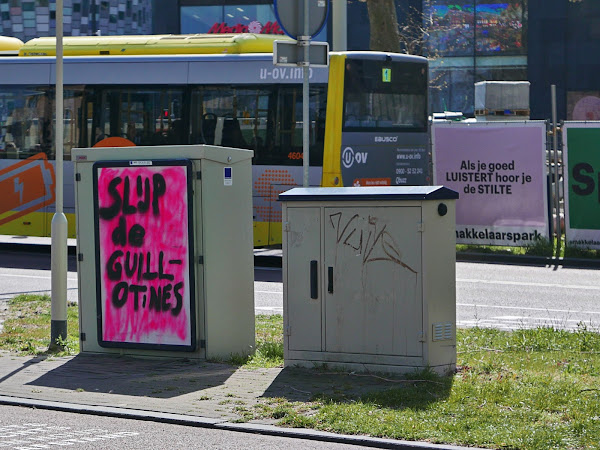 Graffiti 'Slijp de guillotines' naast affiche met de tekst 'Als je goed luistert hoor je de stilte'