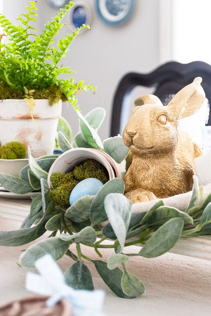 gold rabbit nestled in greenery with pots of eggs and moss