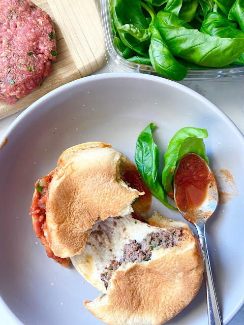 Burger torn in half on a grey plate with spoon, fresh basil and marinara sauce.