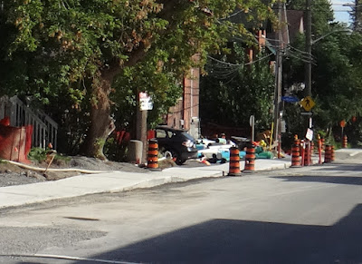 Road under construction with newly built roller coaster style sidewalk. Orange and black traffic barrels along the edge of the roadway. (Lyon Street, west side, south of Gladstone Avenue, during 2016 reconstruction)