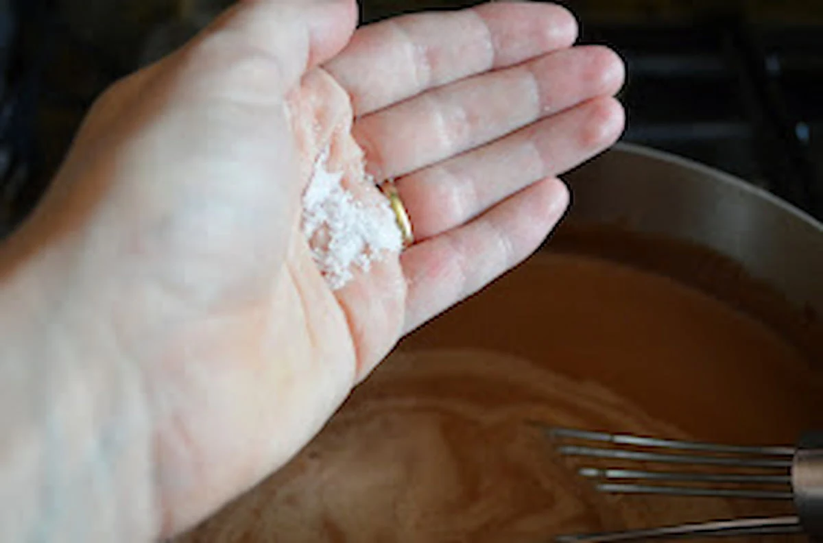 Salt in a hand over chocolate ice cream base in a stainless steel sauce pan.