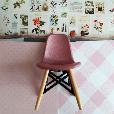 One-twelfth scale pink Eames chair in front of 2 patterns of wallpaper, and an image of a inspiration wall of flowers and birds and photos