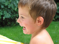 Picture of young, bare shouldered boy on the grass, under a tree, laughing: This is about swimming lessons for 2 year olds