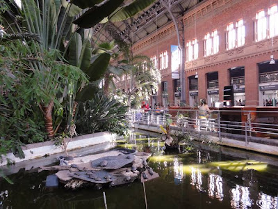 Madrid Atocha (Spanish: Estación de Madrid Atocha, also named Madrid Puerta de Atocha) is the largest railway station in Madrid. It is the primary station serving commuter trains (Cercanías), intercity and regional trains from the south, and the AVE high speed trains from Barcelona (Catalonia), Saragosse (Aragon), Seville (Andalusia) and Valencia (Levante Region). These train services are run by the Spanish national rail company, Renfe. The station is in the Atocha neighborhood of the district of Arganzuela. The original façade faces the Plaza del Emperador Carlos V, a site at which a variety of streets converge, including the Calle de Atocha, Paseo del Prado, Paseo de la Infanta Isabel, Avenida de la Ciudad de Barcelona, Calle de Méndez Álvaro, Paseo de las Delicias, Paseo de Santa María de la Cabeza, and Ronda de Atocha.