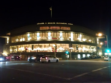 Davies Symphony Hall, a concert hall with large glass windows and a curved corner, lit up at night.