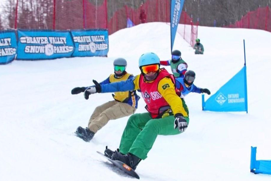 Noah Bethonico, do Snowboard brasileiro, com colete vermelho e camisa amarela, aparece na frente de outros três competidores na neve