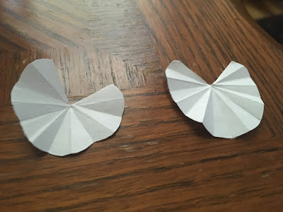 Two small three-quarter-circles of paper with creases radiating from the center to the edges, resting on a wooden table.