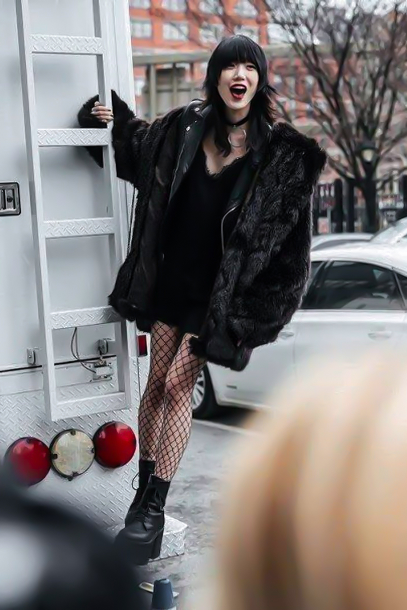 beautiful young woman in a punk black dress and a fishnets tights is posing for the camera on a street
