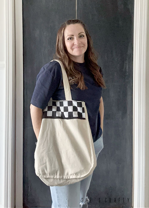 Woman holding canvas handbag with checkered stripe.