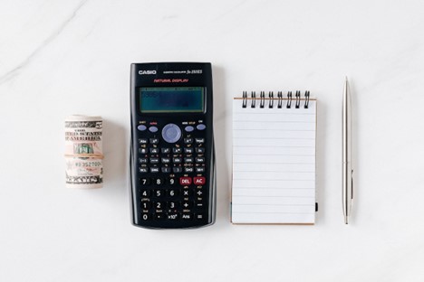 A bundle of dollars, a calculator, a notepad, and a pen.