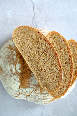 Knuspriges Dinkel-Kartoffel-Brot liegt aufgeschnitten auf grauem Hintergrund, die feinporige Krume ist sichtbar.
