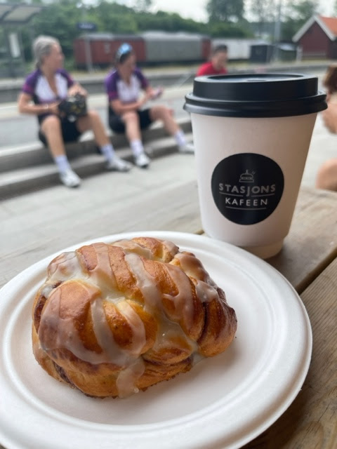 Nærbilde av kanelbolle på papptallerken med en pappkopp med kaffe bak