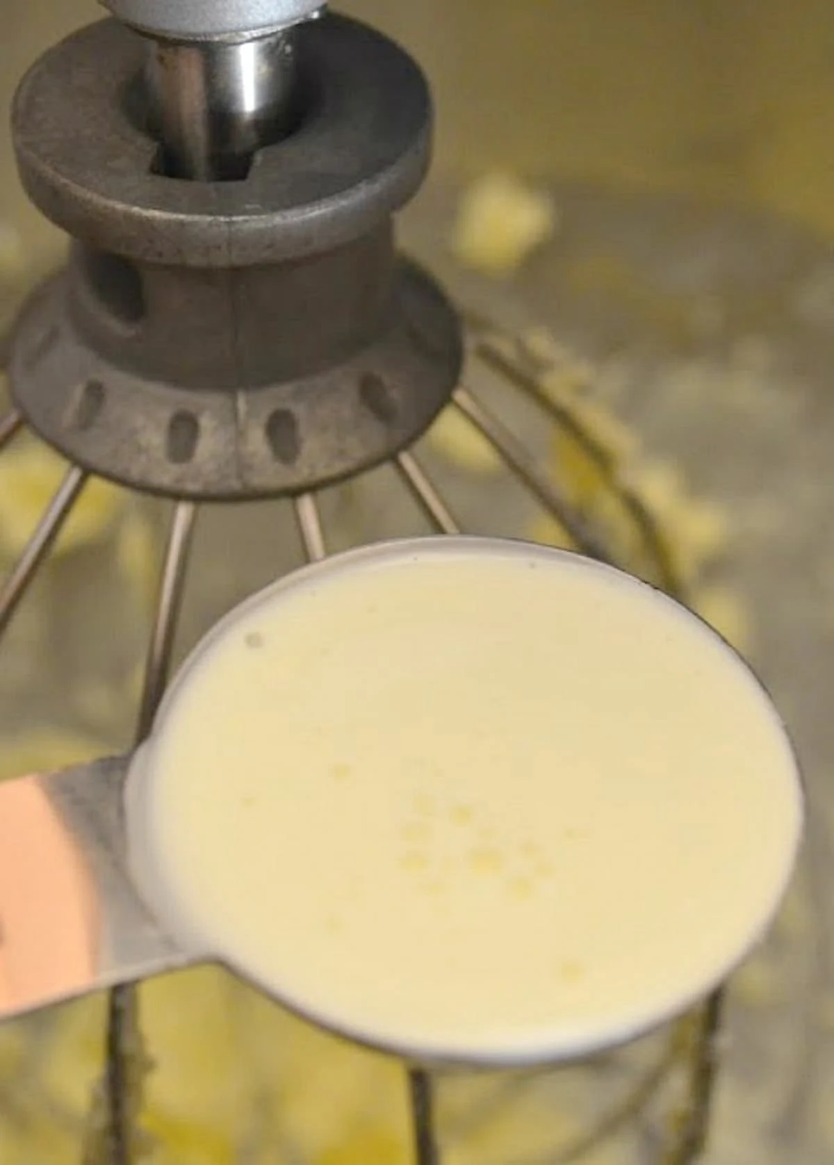 A tablespoon of heavy cream held over a stainless steel mixing bowl with creamed butter.