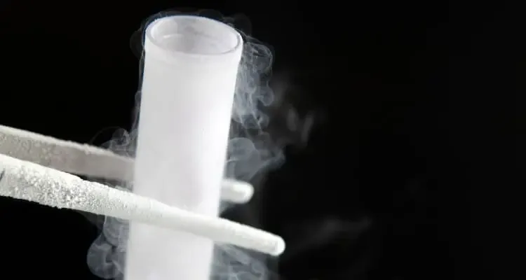 Στην φωτογραφία υπάρχει ένας παγωμένος γυάλινος δοκιμαστικός ιατρικός σωλήνας ο οποίος περιέχει υγρό άζωτο που τον συγκρατεί μια παγωμένη ιατρική τσιμπίδα, σε μαύρο φόντο.