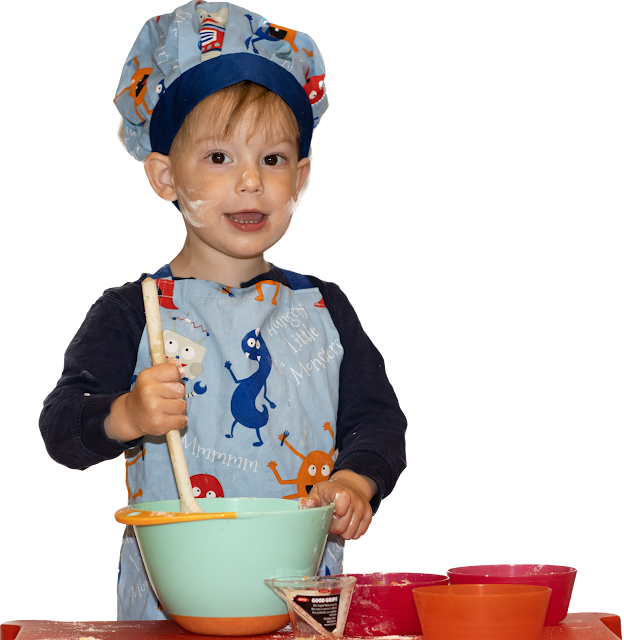 A young child in apron and chefs hat and flour on his face