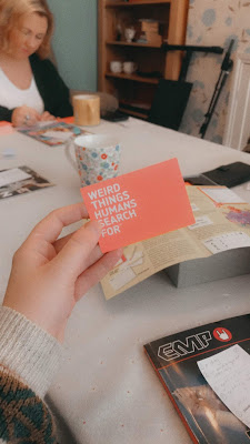 my hand holding a pink games card in front of a dining table