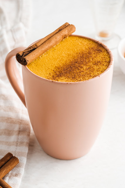 latte in a pink mug with a cinnamon stick garnish.