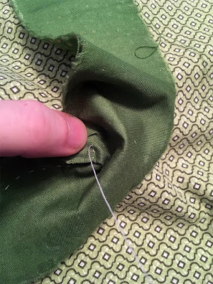 A close-up of the rough pleats being added to the green binding to force it around the tight curve at the bottom of the slit. The binding is being stitched on with white thread.