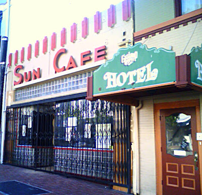 An old cafe Art Deco Cafe.  The building is a beige stucco with a red Art deco sign saying Sun Cafe it also has other Art Deco design elements.