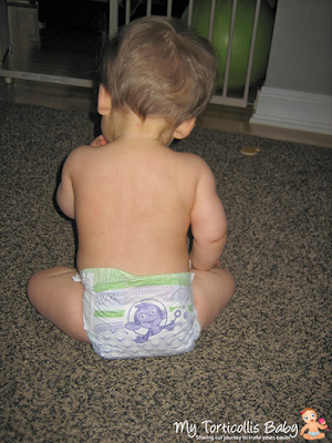 Baby with torticollis sitting on floor and playing with a toy