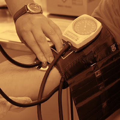 A Nurses hand holding a stethoscope and blood pressure cuff onto an arm while checking blood pressure.