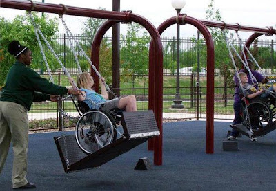 A child in a wheelchair enjoys using a wheelchair friendly swing at a play park.