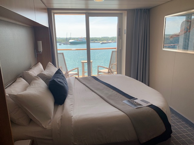 Cruise ship room with a king-sized bed, and balcony in the background