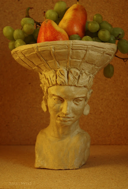 art, sculpture, sarah myers, stoneware, ceramic, escultura, arte, ceramica, fruit, centerpiece, centrepiece, arrangement, figurative, head, woman, basket, bearer, graceful, tranquil, beautiful, food, abundance, plenty, table, face, human, classic, pears, grapes