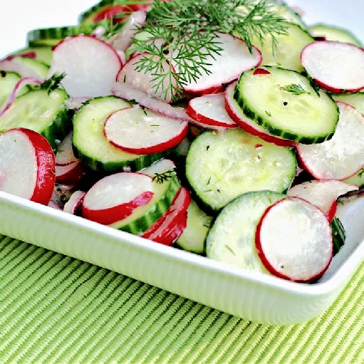 A white plate with dilled cucumber and radish salad on it with a garnish of fresh dill ready to eat.