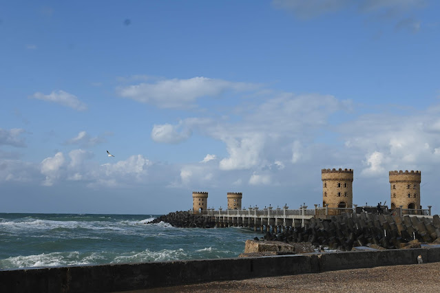 A panoramic view of the new Qaitbay Promenade in Alexandria, Egypt, with visitors walking along the 550-meter sea walkway beside the historic Qaitbay Citadel during sunset.