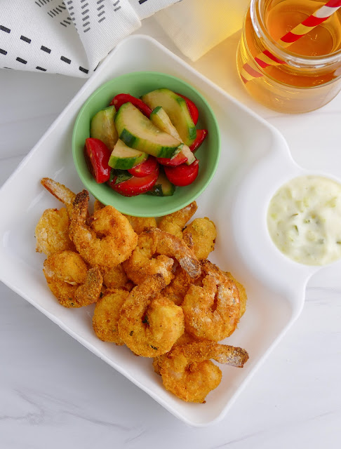 shrimp on a white plate with a salad and tartar sauce on the side.