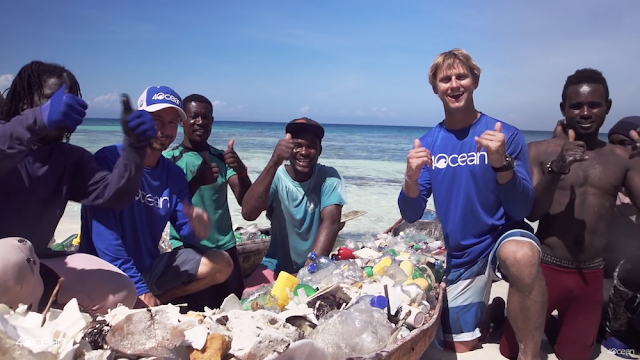 A group of people smiling and kneeling next to a pile of plastic that was taken from the ocean.