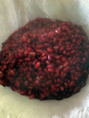 A heaping pile of red, juicy pomegranate arils, slightly obscured by steam, cradled in a doubled layer of white cheescloth.