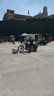Woman riding motorcycle, rolling keg along parking lot with front wheel