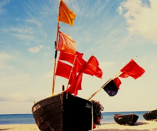 An old wooden fishing boat on the sands with many red flags flying in the wind.