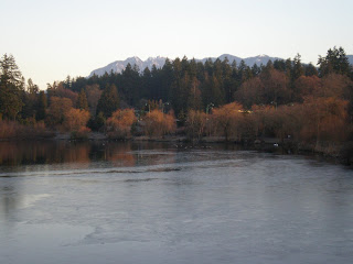 the ice and mountains and trees and clear sky at the lost lagoon near the stanley park entrance