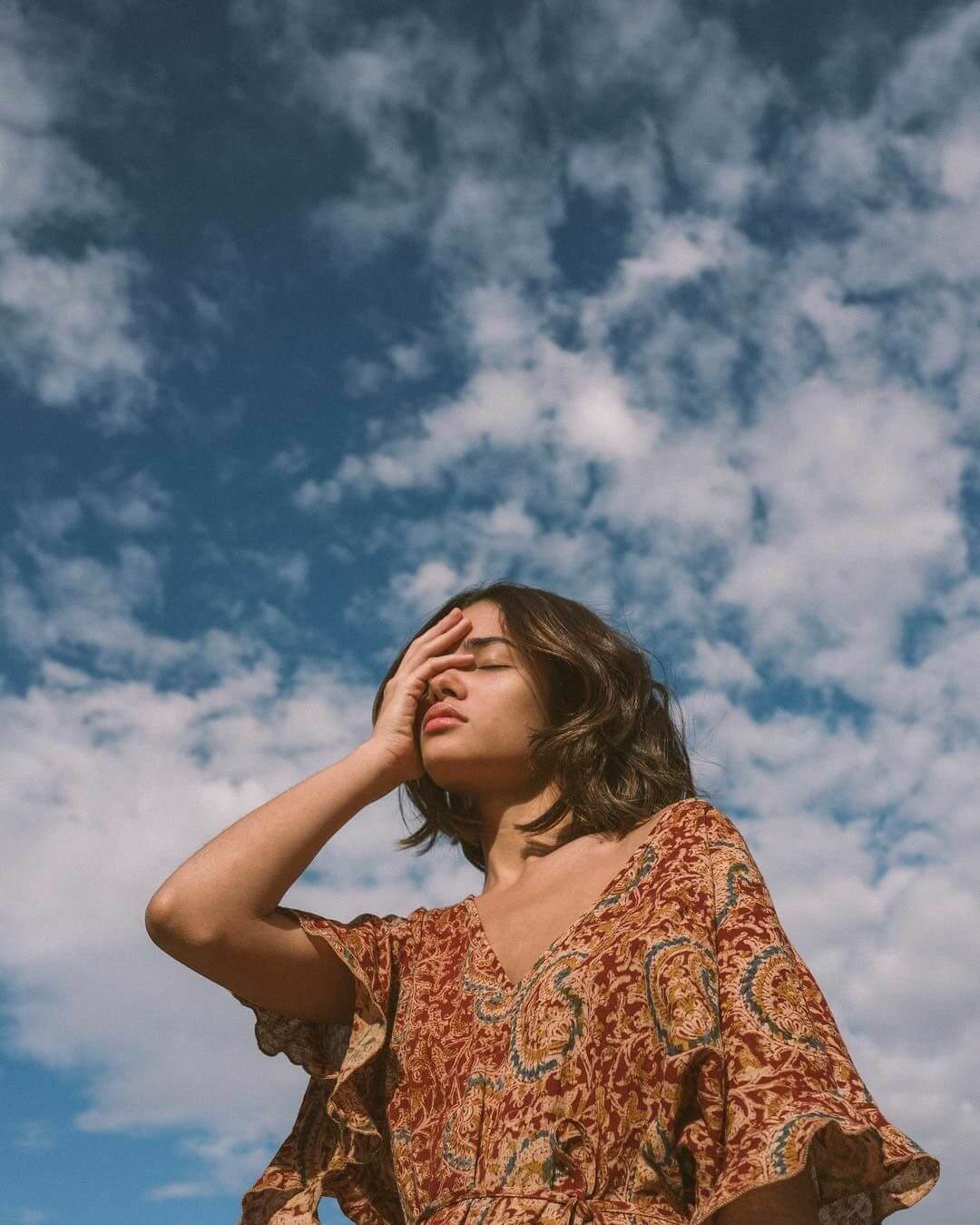 Foto aesthetic chica tapandose la cara con el cielo y nubes de fondo