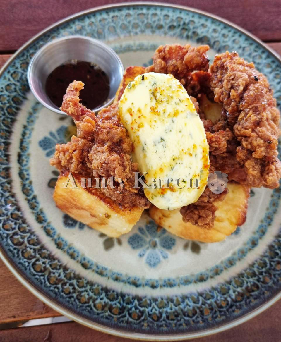 a plate of fried chicken on french toast with a stick of compound better between them and a small metal bowl of maple syrup
