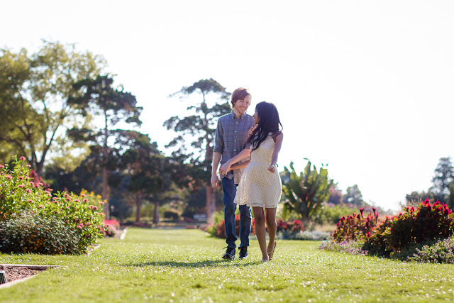 Engaged couple laughing and running hand in hand through a garden of colorful flowers.