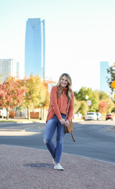 girl smiling with autumn trees and city skyline behind her