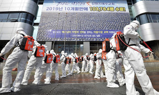 Army soldiers wearing protective suits spray disinfectant to prevent the spread of the coronavirus in front of a branch of the Shincheonji Church of Jesus in Daegu, South Korea, on Sunday. A banner boasts 103,764 have graduated from its program over 10 months in 2019.(Lee Moo-ryul / Newsis )