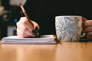 A person writing in a planner with a coffee cup nearby, symbolizing time management and productivity.