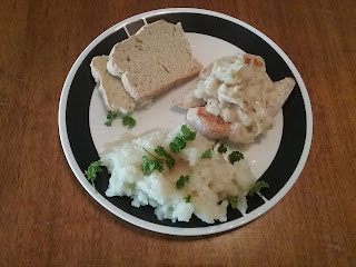 A dinner plate with chicken, mashed potatoes, and bread. A chunky onion sauce is on the chicken. 