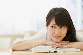 Smiling young woman seated at table resting hands and chin on open hardbound book