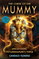 Book cover featuring the golden mask that was with the king in his tomb. There are swirls of light and dusty swirling air around it. The mask is golden with blue accents. There are two snakes up at the forehead.
