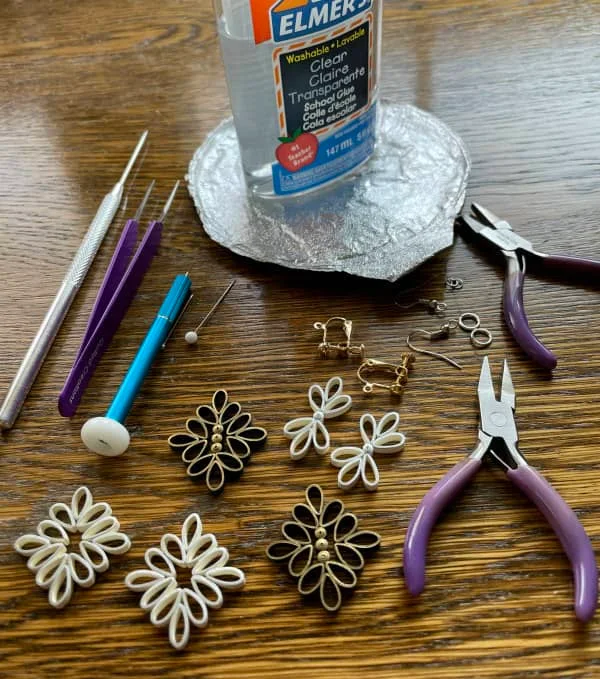 three pairs of quilled earrings displayed with quilling supplies on wooden surface