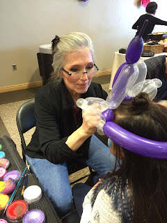 A face painter painting a girls face while she wears a balloon crown