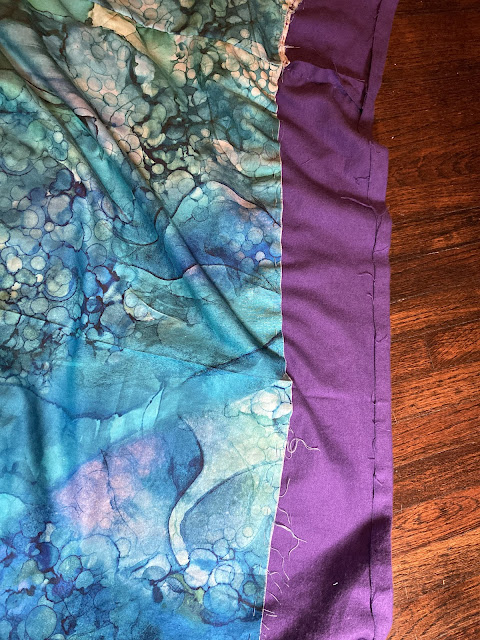 The unfinished blue/green lining of a jacket, with the unfinished bottom edge of purple flannel visible