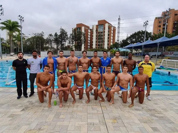 Seleção brasileira sub-20 de polo aquático e comissão técnica posa na frente de piscina para foto.